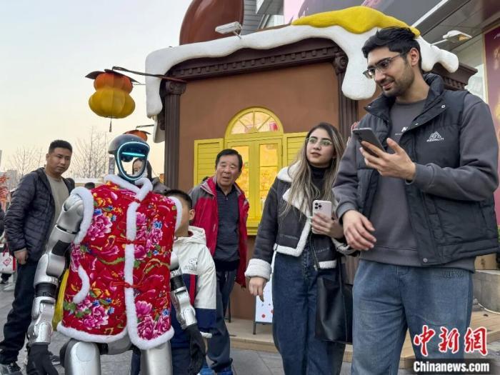 2026年2月14日，人形机器人亮相河南郑州金水区花园路商圈一家商场，吸引不少市民与游客驻足观看。图为人形机器人与外国游客互动。中新社记者 范晓恒 摄