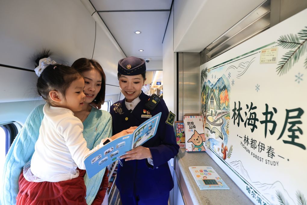 10月4日,在哈伊高铁D7275次列车餐车的林海书屋,“林之馨”品牌班组列车长齐智馨(右)为小朋友讲解儿童读物。新华社发(徐率 摄)
