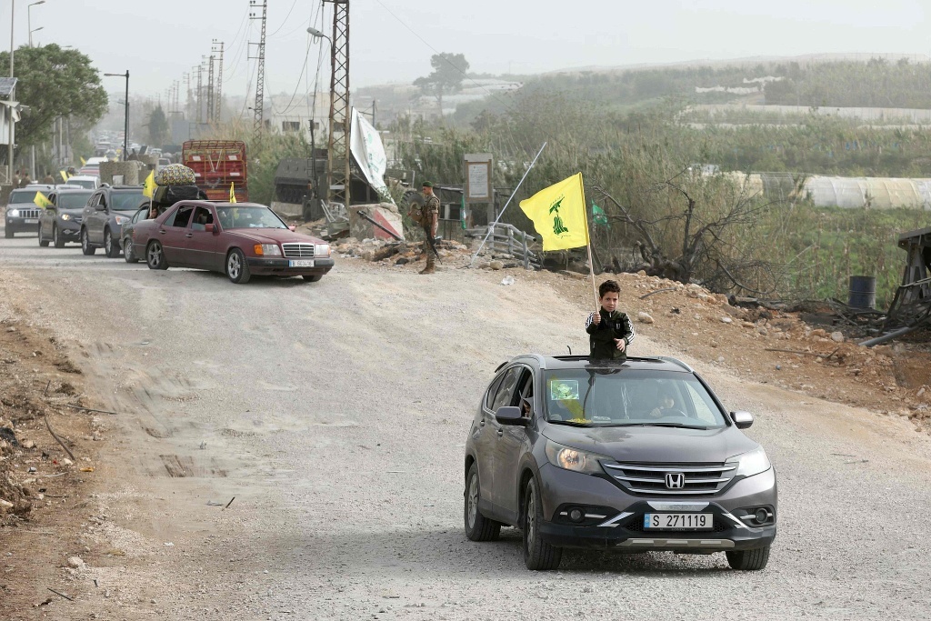 当地时间2026年4月18日，黎巴嫩南部地区，流离失所的居民挥舞着真主党旗帜，通过临时道路返回他们的家园。视觉中国 图