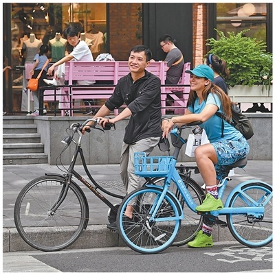 随着“China Travel”走红，越来越多美国游客来中国旅游。图为5月23日，一名美国游客（右）与其入境旅游策划师在上海武康路骑行。新华社记者 陈浩明摄