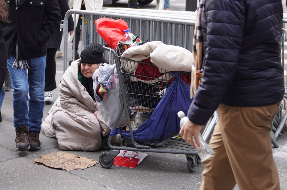 2025年12月31日,在美国纽约街头,无家可归者坐在街边等待帮助。新华社记者张凤国摄