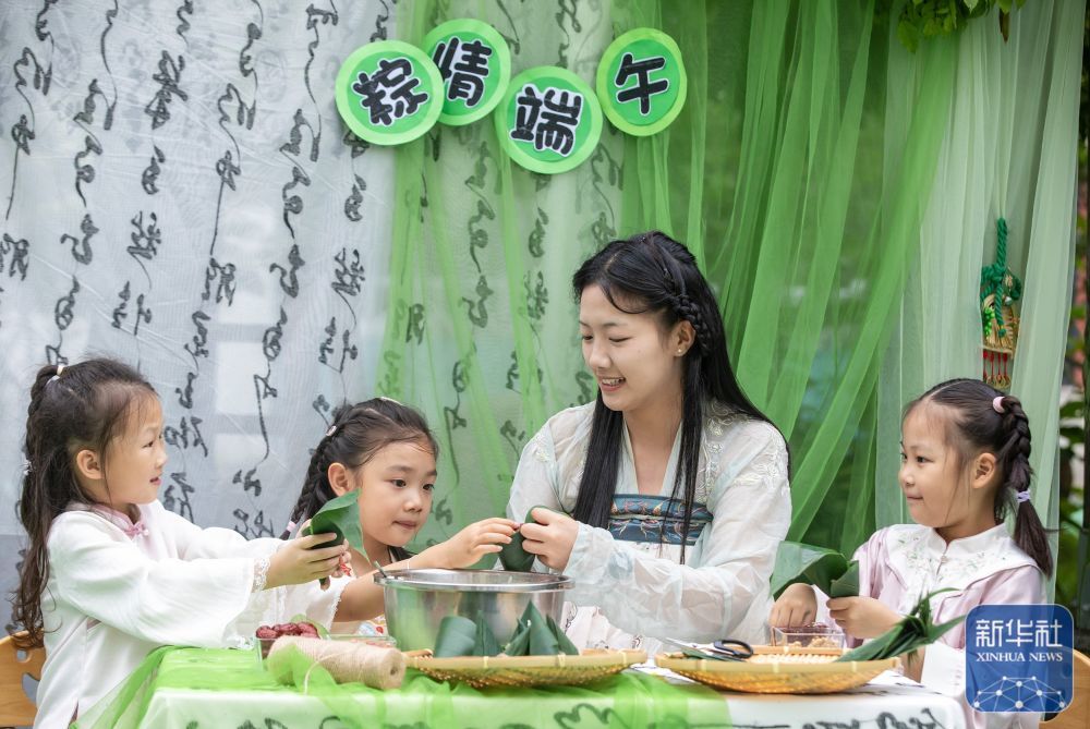 ↑ 6月16日,江苏省南通市通州区通州幼儿园的孩子们在跟着老师学包粽子。新华社发(翟慧勇摄)