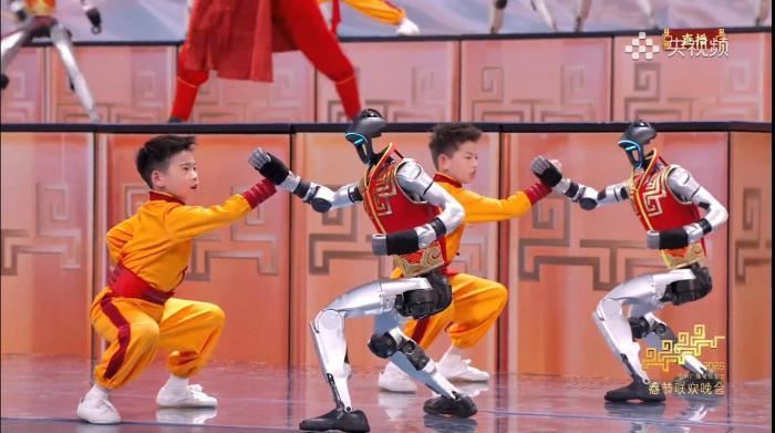由宇树科技机器人与河南塔沟武术学校的小朋友同台呈现的节目《武BOT》中，机器人在和小朋友对练。(央视频截图)