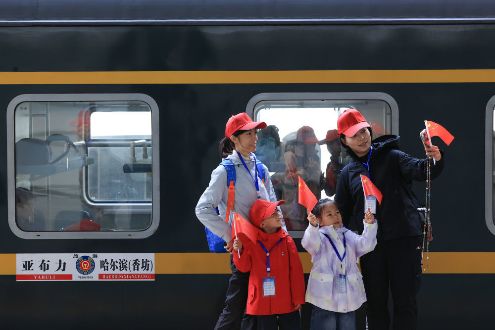 10月1日，旅客在黑龙江哈尔滨站乘车出游前手持国旗合影留念。新华社发（徐率 摄）