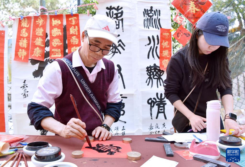 2月13日,在香港楼梯街,萧嘉豪(左)在书写挥春。新华社记者 陈铎 摄