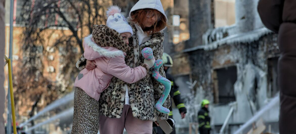 一名母亲带着女儿走过基辅一栋在夜间袭击中受损的工业建筑。(来源:联合国网站)