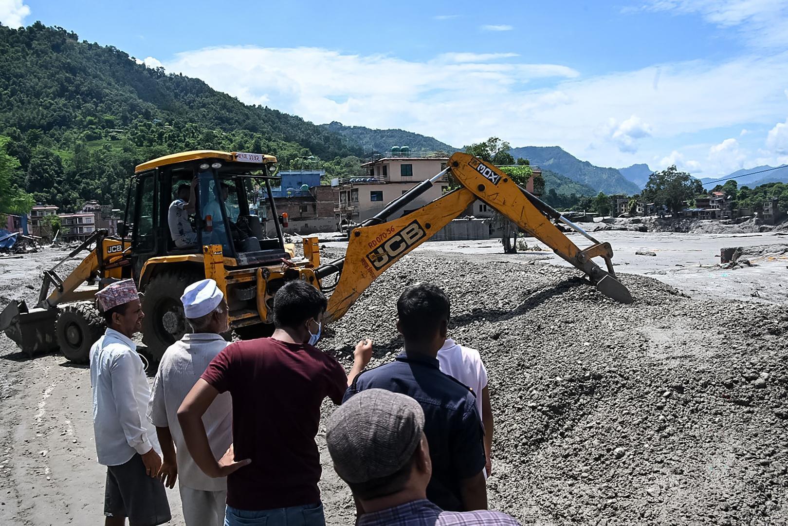 ▲当地时间2026年8月27日,尼泊尔努瓦果德县德维加特地区,居民聚集在道路旁,工人使用推土机清理山洪暴发后的泥浆和碎石(图据视觉中国)