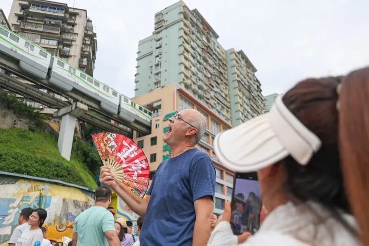 8月10日，在重庆市渝中区李子坝观景平台，外籍游客摆出“吃”轻轨的姿势拍照。新华社记者 黄伟 摄