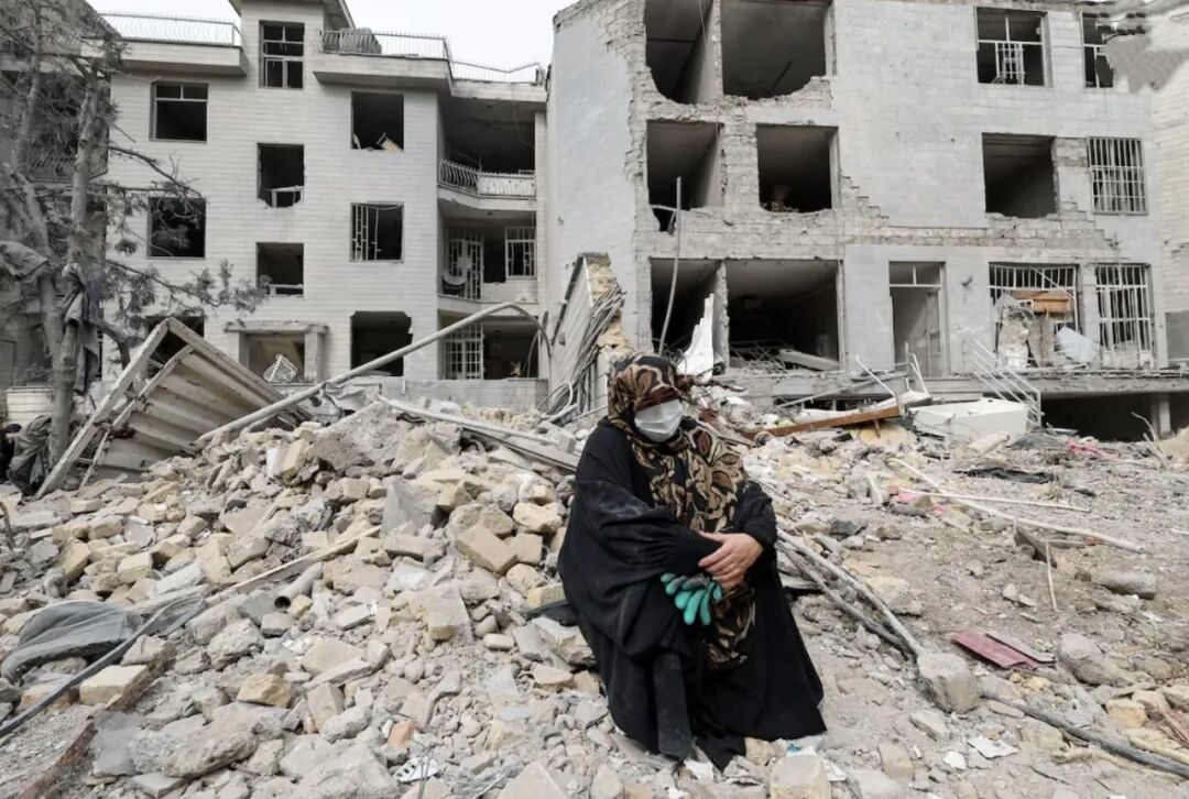 ▲3月12日，在伊朗德黑兰，一名女子坐在被空袭摧毁的公寓外。（图源：路透社）
