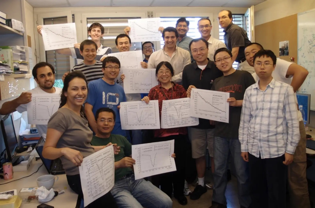 2012年希格斯玻色子被发现时，威斯康星大学麦迪逊分校ATLAS 团队正在欧洲核子研究中心（CERN）。确认信号达到 5σ（5西格玛） 后，团队成员拿着数据图合影庆祝。图源：威斯康星大学麦迪逊分校