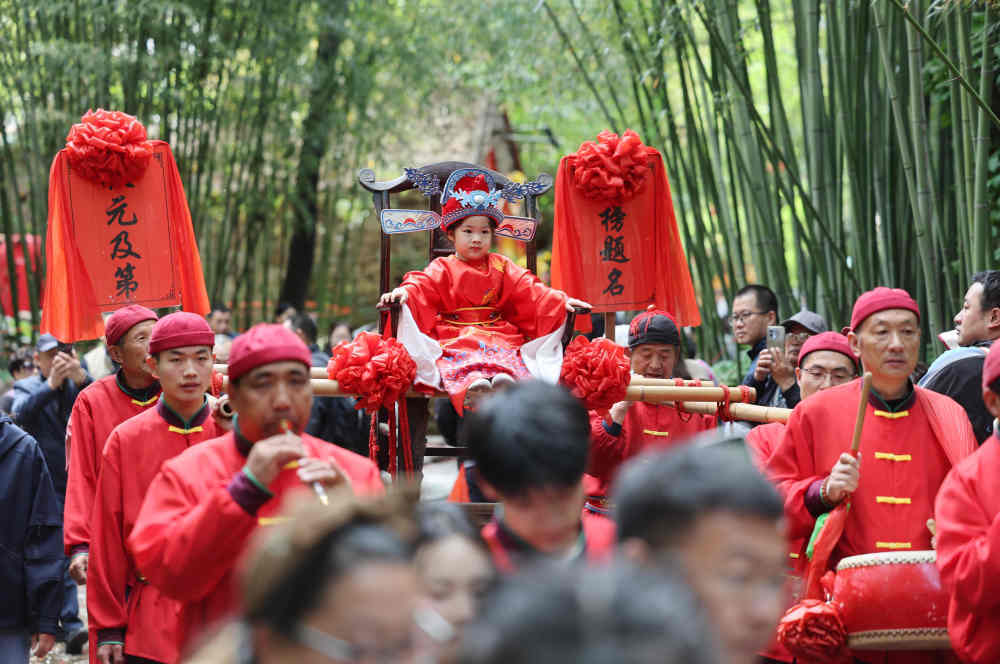 ↑ 5月3日，在山东省临沂市沂南县铜井镇竹泉村，游客参与体验高中“状元”表演。新华社发（王彦冰摄）