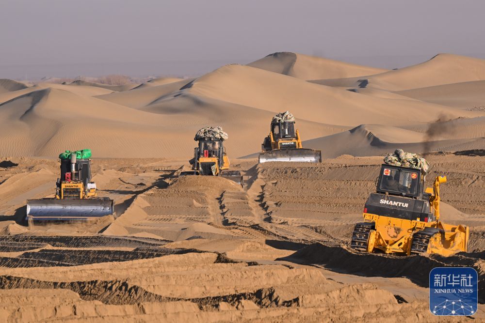↑ 在新疆和田地区墨玉县喀瓦克乡，大型机械在沙漠中穿梭作业、平整沙地（1月11日摄）。
