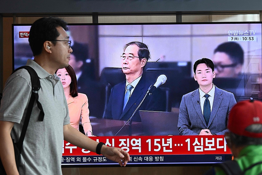 5月7日，韩国首尔，一名男子走过火车站内播放前韩国总理韩德洙涉协助戒严案庭审直播的电视屏幕。（视觉中国）