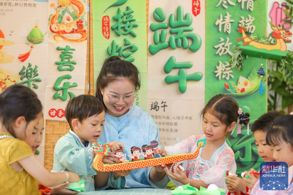 ↑ 6月17日,在山东省青岛市李沧区青山路幼儿园开展的“巧手承古韵 欢乐过端午”主题活动中,老师指导小朋友拼插龙舟模型。新华社发(张鹰摄)