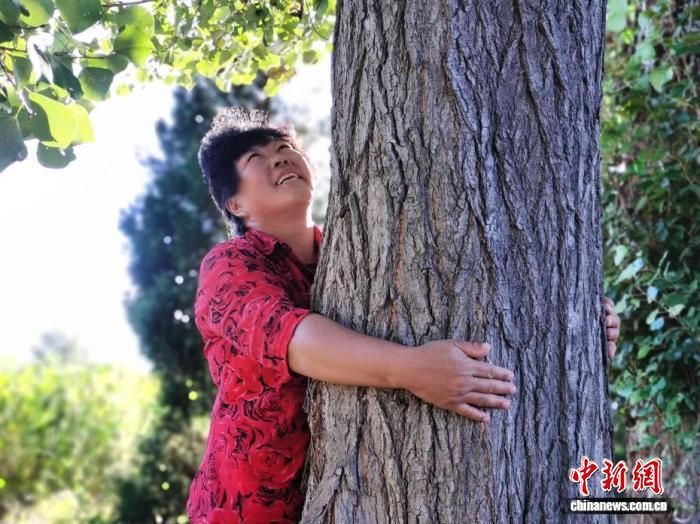 内蒙古毛乌素沙地，用了30多年，绿化了6万多亩荒沙的殷玉珍与亲手种植的树木拥抱。党田野 摄