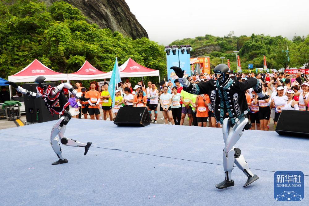 ↑ 6月20日,在重庆市黔江区小南海景区,机器人在一项跑步活动现场表演。新华社发(杨敏摄)