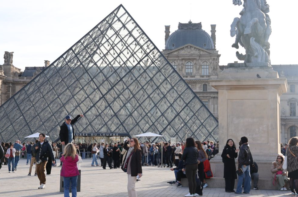 2025年10月22日，在法国巴黎，大量游客聚集在卢浮宫博物馆的玻璃金字塔入口前。图源：新华社