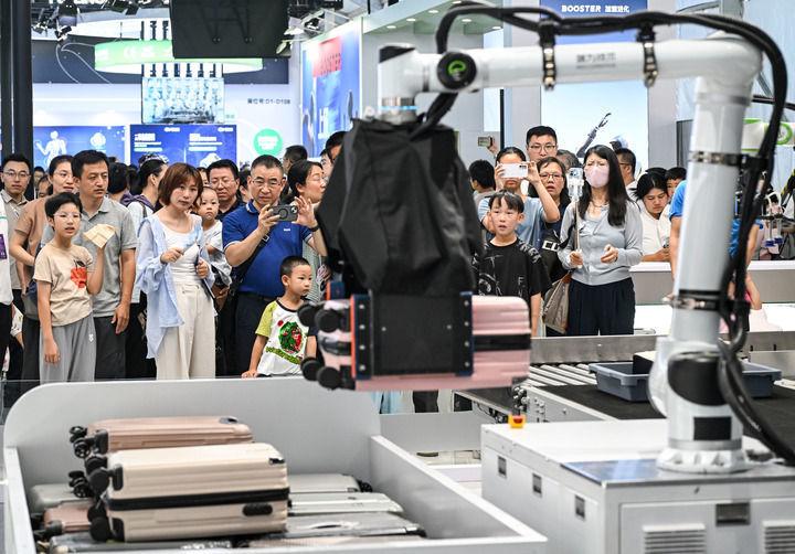 8月22日,观众在2026世界机器人大会上观看一款机械臂搬运行李箱过安检机。(陈晔华 摄)