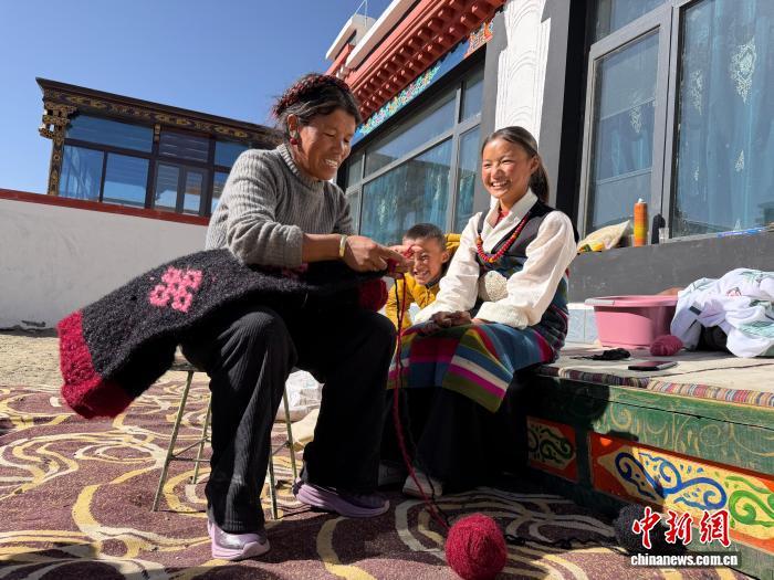 1月5日,森嘎村的卓玛(左一)在院子里晒着太阳织毯子。中新社记者 赵朗 摄
