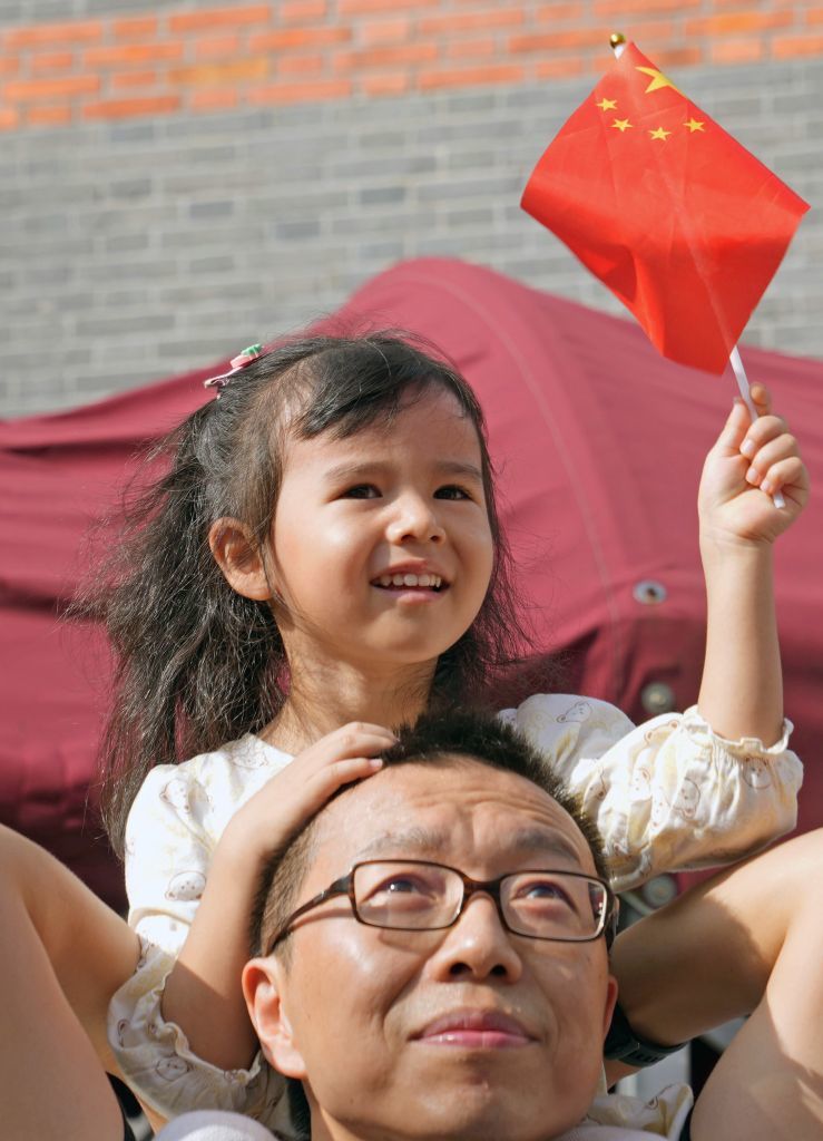 2025年10月1日,在上海中共一大纪念馆,一名小女孩坐在爸爸的肩膀上观看升旗。新华社记者 刘颖 摄