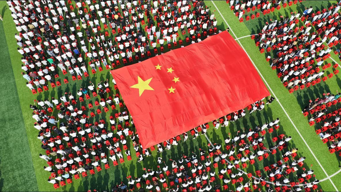 图为新生们接力传递巨幅国旗 摄影:金天.png
