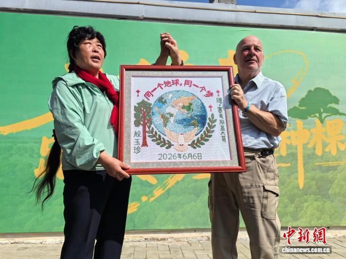 8月25日,内蒙古鄂尔多斯市乌审旗,中国“治沙劳模”殷玉珍与美国友人“赛考斯”交换礼物。图为殷玉珍赠送“赛考斯”一幅十字绣。 中新社记者 曾玥 摄