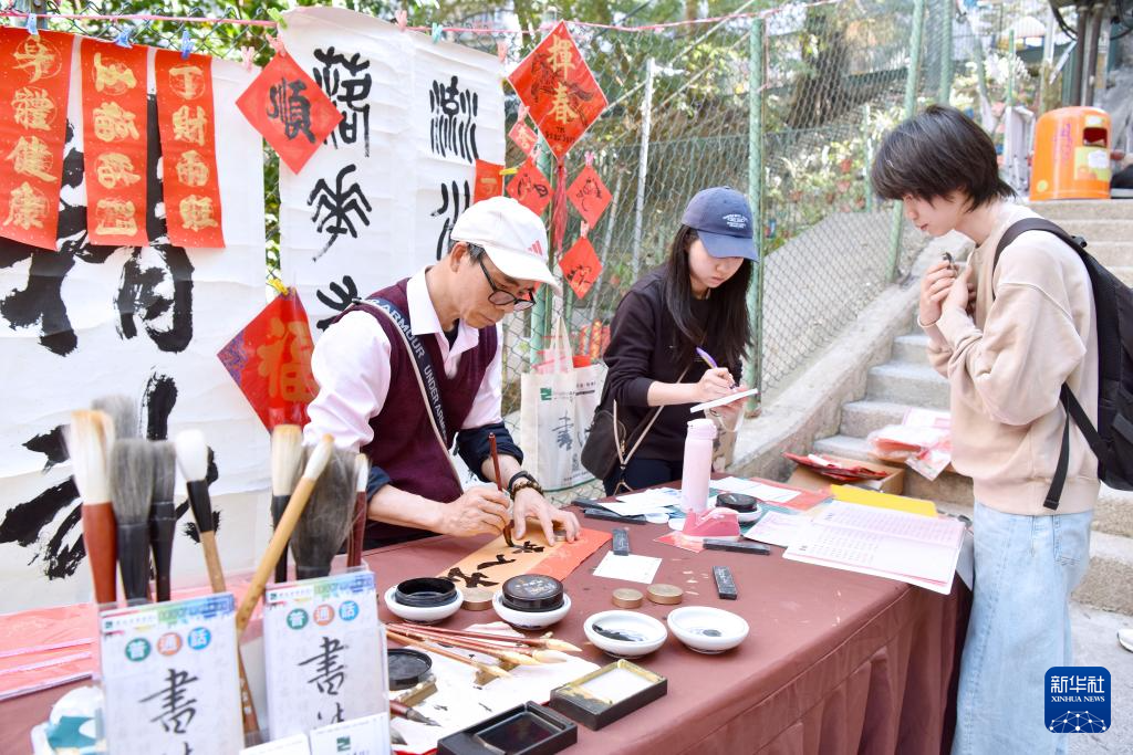 2月13日,在香港楼梯街,萧嘉豪(左)在书写挥春。新华社记者 陈铎 摄