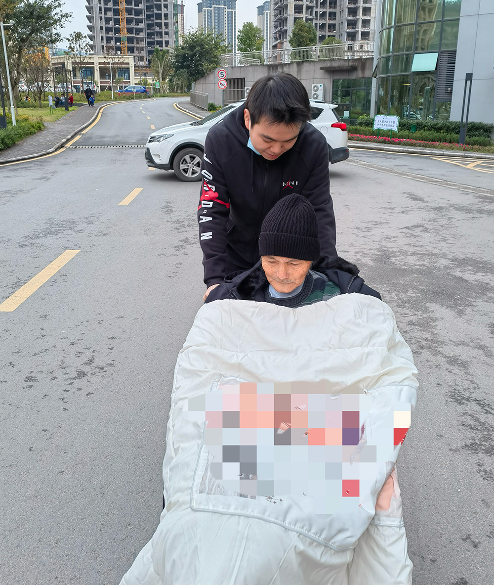 患病后的吴德明(戴帽者)靠坐轮椅出行。