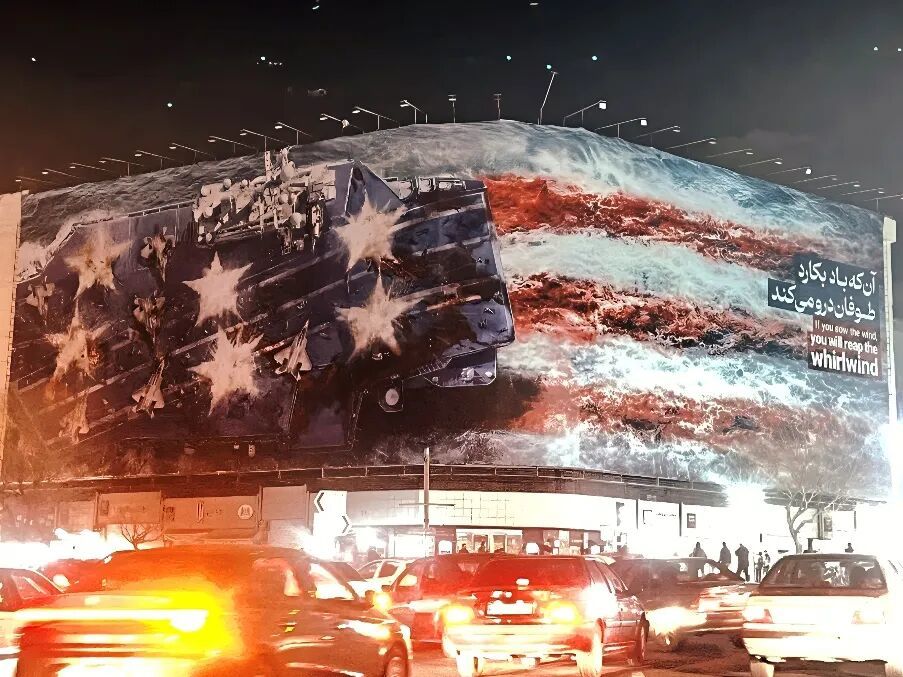 德黑兰市中心革命广场,高悬的“纵火者终将自焚”巨幅海报占据街景,画面中美国军舰被击沉于海浪之中