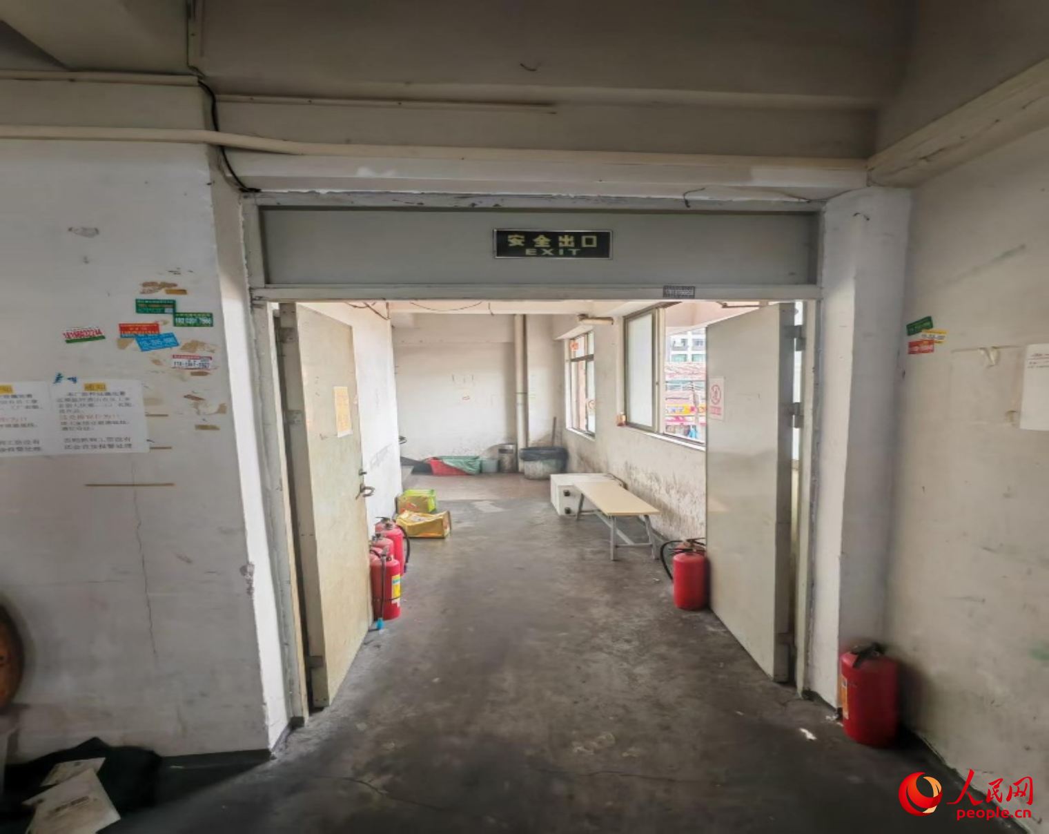 被灭火器抵住敞开的常闭式防火门，门口还扔有两个装过强力清洁剂和衣车油的空桶，疏散通道还堆有其它杂物。人民网记者 王子锋摄