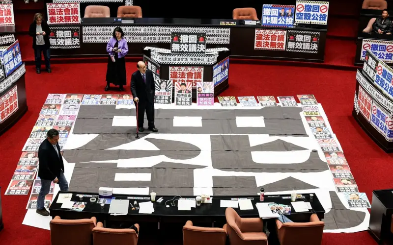 2025年3月28日,民进党立委站在立法院一张写有“罢免”字样的海报上(图源:法新社)