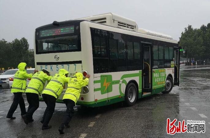 图为交警帮助雨中出故障的公交车重新启动。