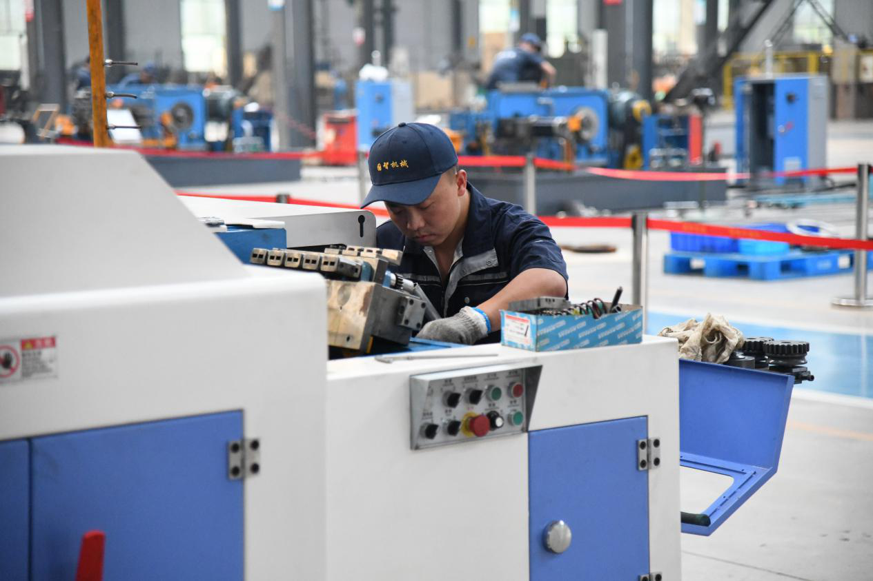 图为河北国智机器设备制造有限公司车间，工人对冷镦机进行组装调试