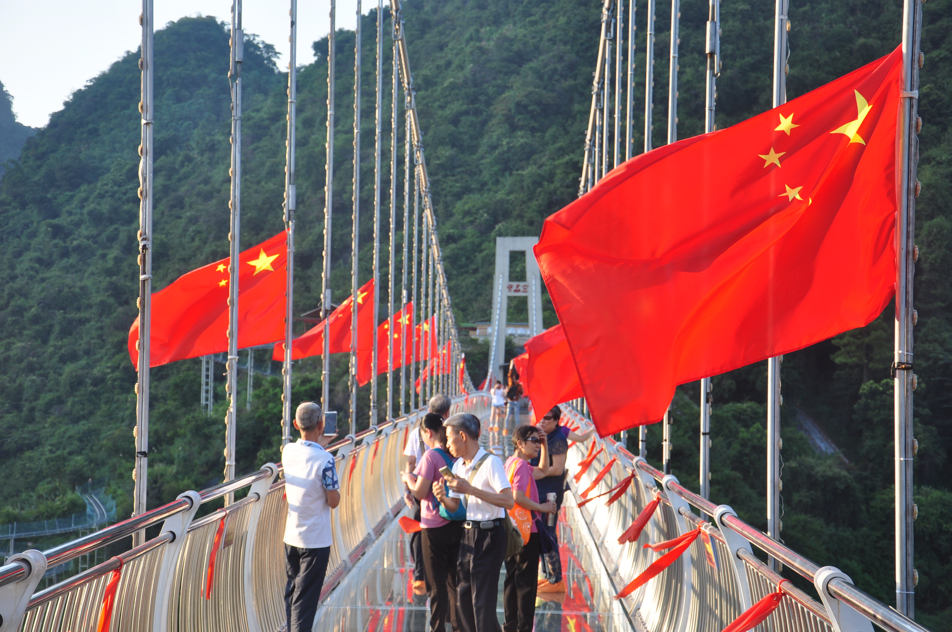 游客走在飘着红旗的玻璃桥上