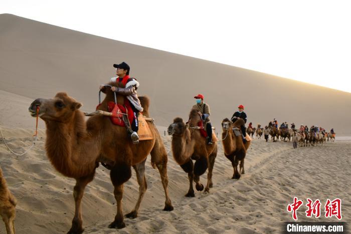 夕阳西下，游客骑骆驼畅游鸣沙山，欣赏敦煌大漠秋景。　王斌银 摄