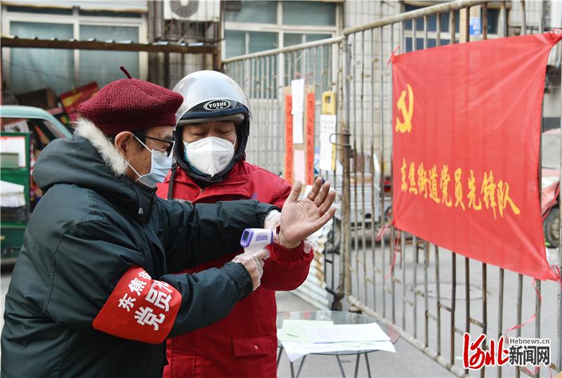2月7日，石家庄市东焦街道红军大街社区新闻里7号院门口，80岁的老党员李乃秋在为出入小区的居民测量体温。 河北日报记者赵海江摄