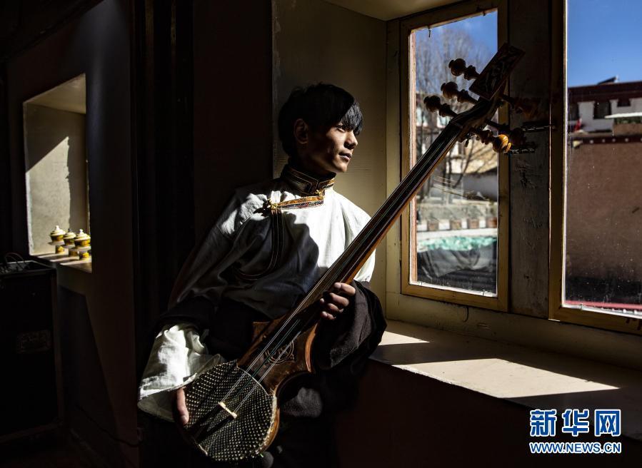 在理塘县勒通古镇的喜马拉雅之声微博物馆，丁真抱着藏族传统乐器——扎木聂，望着窗外的古镇街巷（12月2日摄）。在这个微博物馆，游客可以体验藏族传统乐器，聆听马蹄声等声响，观看藏族传统音乐相关的视频。当地通过老城区改造等一系列措施，打造出著名景区“千户藏寨”，包括勒通古镇、仁康古街、长青春科尔寺等，集中展现理塘的历史文化魅力。这里将成为丁真未来的工作场所之一。