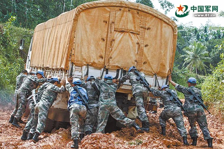 中国赴利比里亚维和部队运输分队官兵在泥泞的道路上推车。