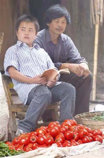 2006年7月，覃甫政和他的父亲坐在家门口的一个菜摊前。