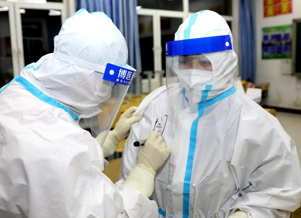 在固安县东湾乡苏桥中学核酸检测采集点，一名医护工作者为同事在防护服写上名字。