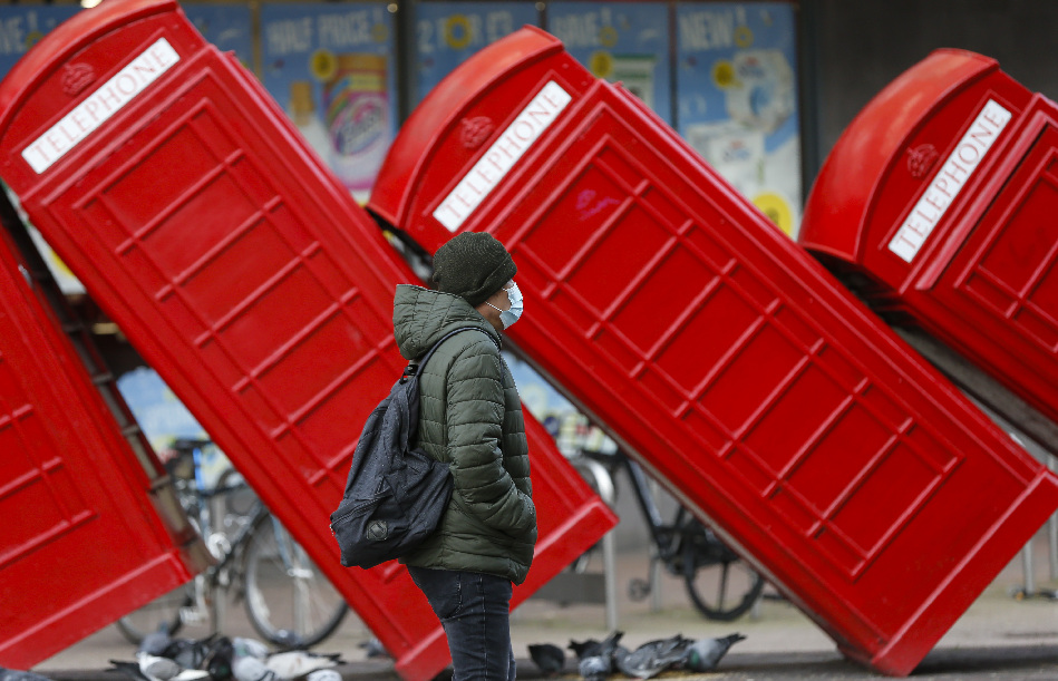1月21日，一名戴口罩的男子从英国泰晤士河畔金斯顿街头的红色电话亭雕塑旁走过。 新华社记者 韩岩 摄