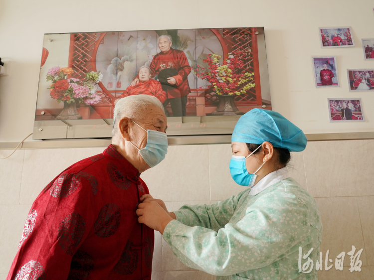 2021年2月10日，在河北省邢台市巨鹿县福缘居医养中心，护工为师英灿老人（左）穿新衣。