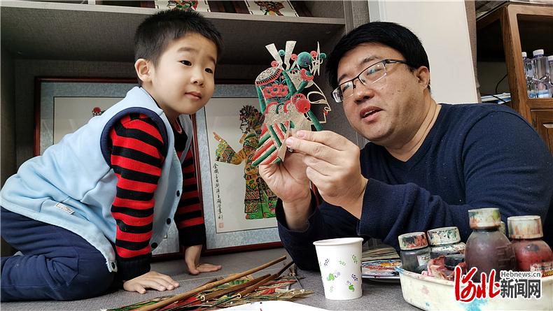 4岁的涵涵（左）饶有兴趣地观看爸爸周学军雕刻皮影人。河北日报记者汤润清摄