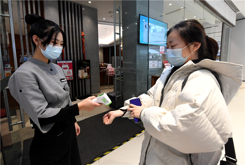 工作人员(左)为准备进店的顾客测量体温