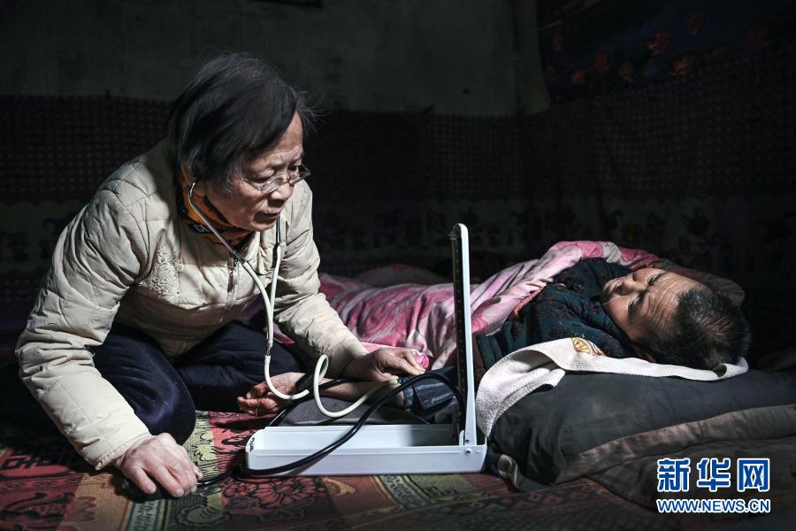 在佳县店镇贺家沟村农家窑洞里，路生梅跪坐在土坑上为瘫痪不起的66岁村民乔爱芬义诊（1月18日摄）。新华社记者 陶明 摄