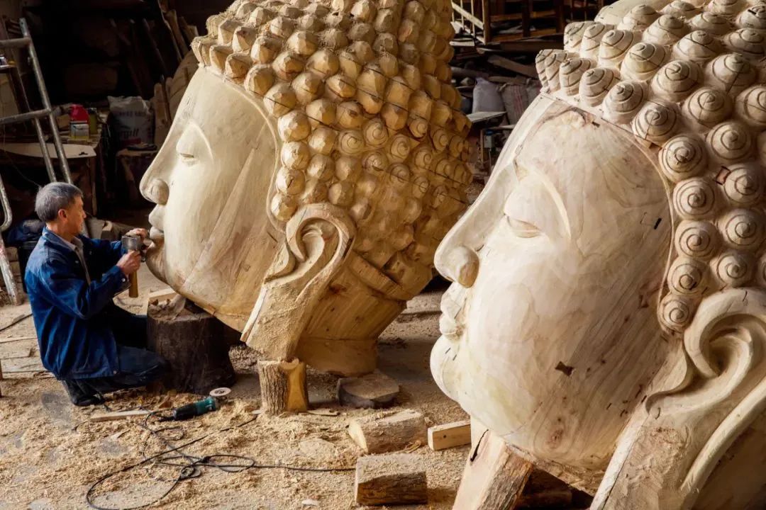 ▲在浙江台州市天台县的某个佛雕工厂，工匠正在对两尊巨大的佛像头部进行最后的雕凿。摄影/王小红
