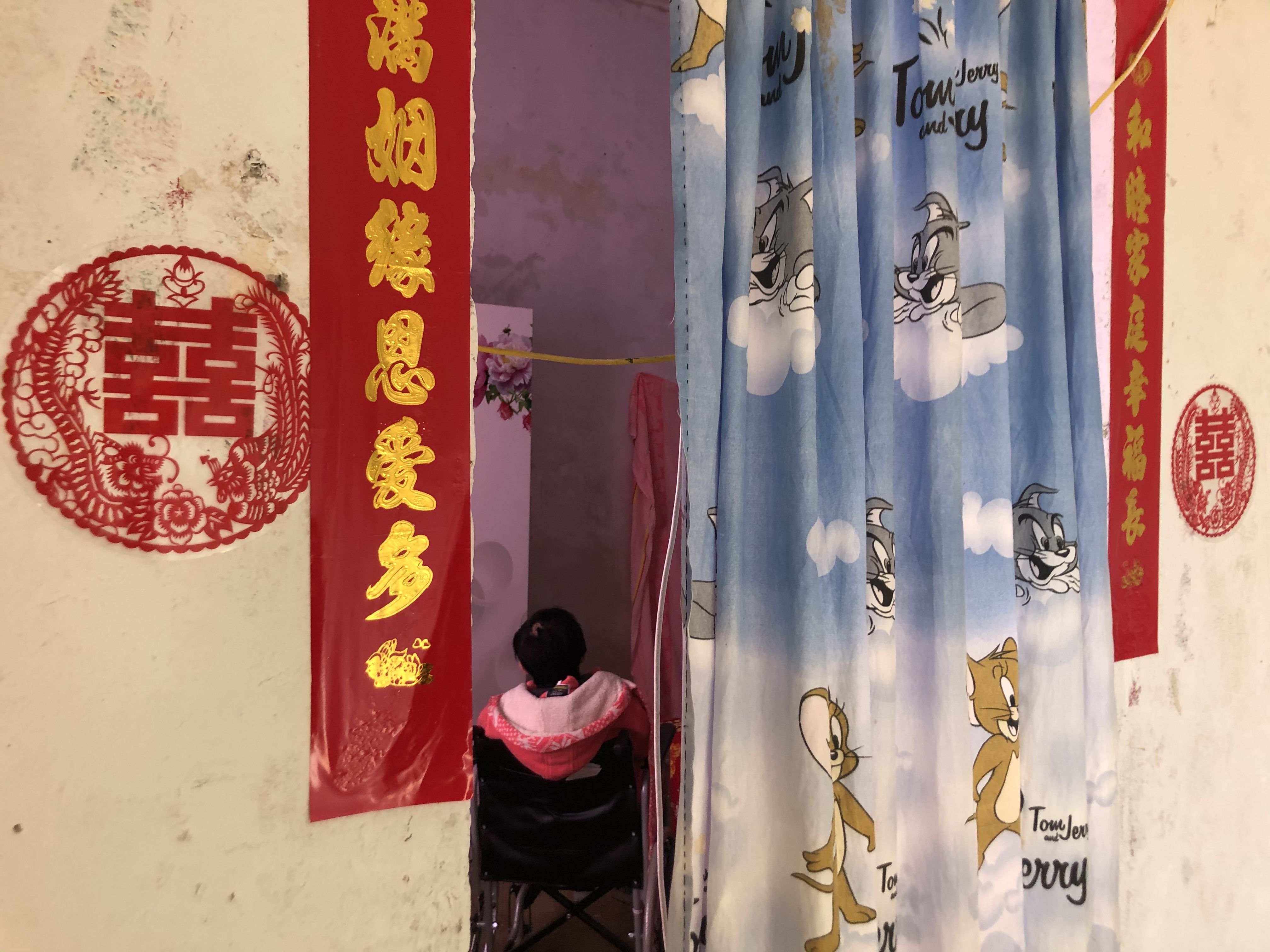 新娘坐在婚房的轮椅上，门口贴着新婚对联。新京报记者 杜寒三 摄