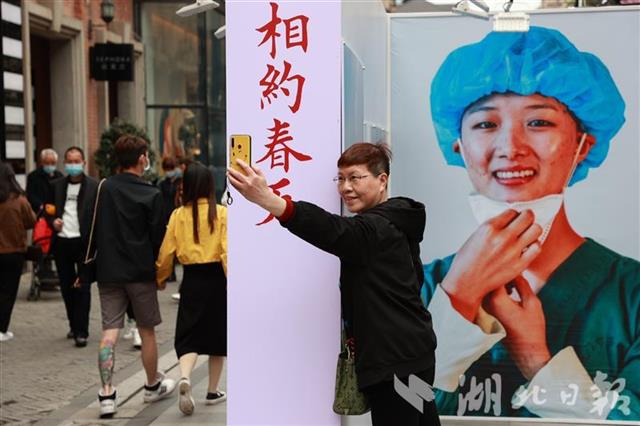 2021年4月10日，一位市民在楚河汉街“相约春天”抗疫摄影展板前留影。