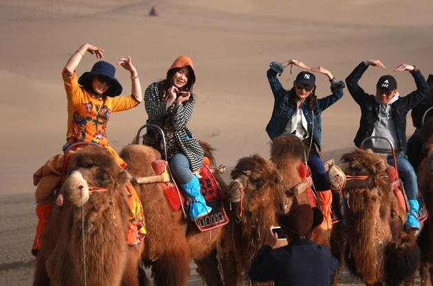 2021年5月3日，在甘肃省敦煌市鸣沙山月牙泉景区，游客和骆驼合影。