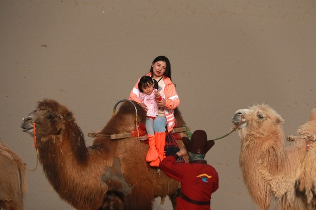 2021年5月3日，游客乘骑骆驼在甘肃省敦煌市鸣沙山月牙泉景区游览。